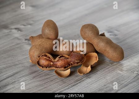 Rustikale Szene einer Gruppe von braunen süßen Tamarinden, die sich auf einer Holzoberfläche mit verschiedenen Grautönen verteilen Stockfoto