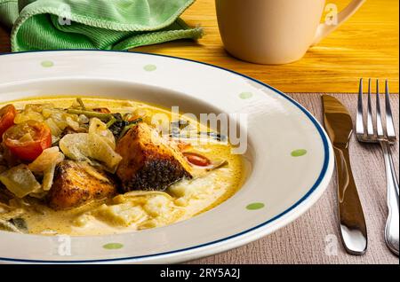 Gerösteter Lachs mit Kartoffelpüree, Tomaten und Spinat in weißer Keramikplatte mit Metallmesser und Gabel auf Tischmatte. Stockfoto