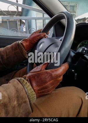 Hände des Menschen am Lenkrad in Lederhandschuhen beim Autofahren im Winter. Nahaufnahme. Selektiver Fokus. Stockfoto