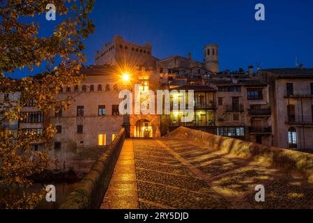 Burg und Kirche von Valderrobres, beleuchtet zur blauen Stunde und in der Nacht, von der Brücke über den Fluss Matarraña (Teruel, Aragon, Spanien) aus gesehen Stockfoto