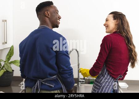 Glückliches, abwechslungsreiches Paar, das zu Hause in der Küche Geschirr macht Stockfoto