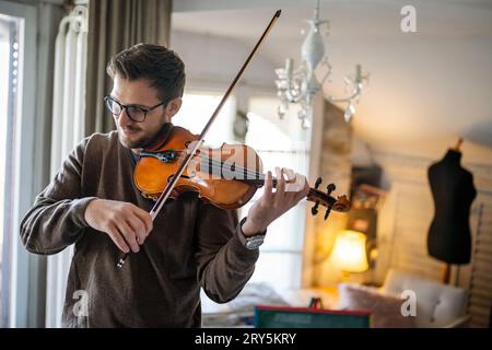 Junger weißer Mann, der zu Hause Geige spielt. Hobby Quality Time Happiness Konzept. Stockfoto