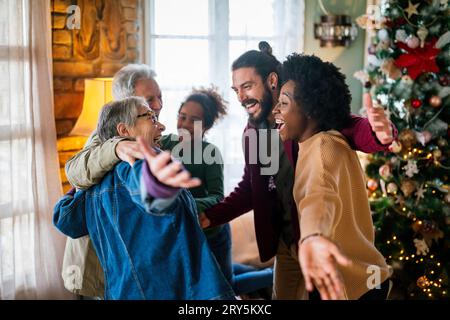 Aufgeregte multiethnische Familie begrüßt Großeltern am ersten Weihnachtsfeiertag. Eine glückliche Familie für mehrere Generationen Stockfoto