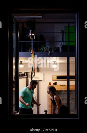 Fit Mädchen mit Training mit Seilen mit einem männlichen Fitness-Trainer in einem Fitness-Studio. Blick von außen. Stockfoto