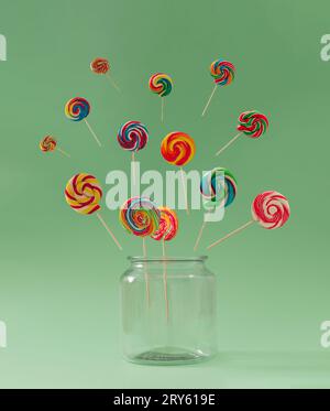 Bunte Lutscher aus dem Glas vor pastellgrünem Hintergrund. Kreatives Süßigkeitenkonzept. Minimaler Lutscher. Stockfoto