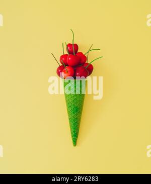Rote Kirschfrucht in grünem Kegel auf pastellgelbem Hintergrund. Minimales Sommerfrucht-Konzept. Kreative Sommereis-Idee. Flache Kirschanordnung. Stockfoto