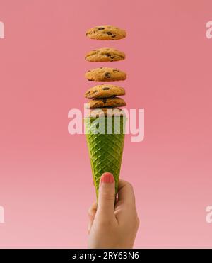 Grüne Waffel-Eiskegel mit Schokoladenkeksen auf hellrosa Hintergrund. Minimales Lebensmittelkonzept. Kreative Idee für den Sommer. Leckerer Schokoladen-Kekschip. Stockfoto