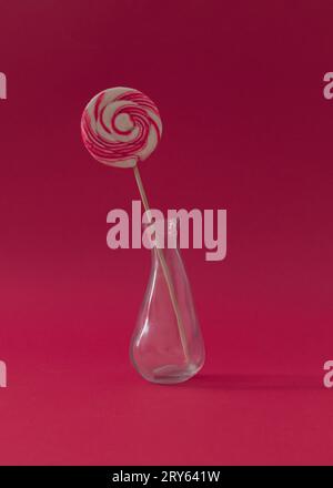 Lutscher als Blume in einer Vase vor rotem Hintergrund. Sommerbonbons-Konzept. Kreative, süße Idee. Stockfoto