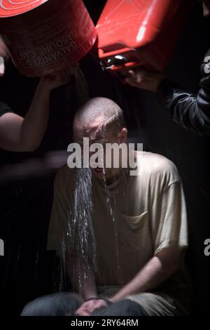 Zwei rote Dosen Benzin werden auf einen sitzenden Mann gegossen. Stockfoto