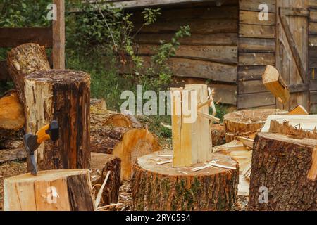 Fotoaufnahme von Holzaufbereitungsarbeiten für Lagerfeuer in der Natur. Trockener, großer Baumstamm auf dem Baumstamm, umgeben von Sägemehl, vor dem Landhaus, W Stockfoto