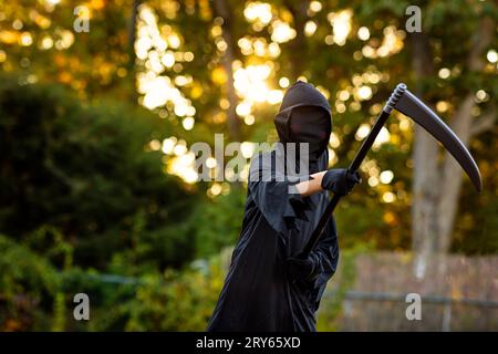 Tween verkleidet als der grimmige Sensenmann, der zu halloween eine Sense hält Stockfoto