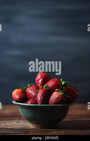 Reife Erdbeeren in grauer Schüssel dunkler Moody Blue Hintergrund Stockfoto