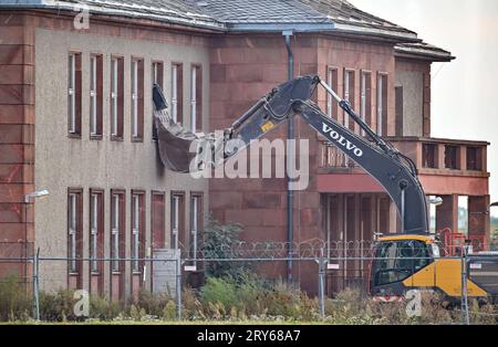 29. September 2023, Brandenburg, Schönefeld: Ein Bagger steht vor dem für den Abbruch vorgesehenen General Hotel auf dem ehemaligen Flugplatz Schönefeld, dem heutigen Flughafen Berlin Brandenburg (BER). Die Vorbereitungen für den Abriss des historischen Generalshotels auf dem Gelände des BER-Flughafens werden trotz starker Proteste von Politikern, Architekten und Denkmalschützern fortgesetzt. Nach Angaben der Bundesbehörde soll der Abriss Anfang 2024 abgeschlossen sein. Foto: Patrick Pleul/dpa Stockfoto