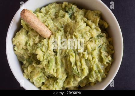 Ein Makroschuss eines köstlichen, hausgemachten Guacamole-Dips in einer runden Schüssel, garniert mit einem knusprigen Vollkornbrettich. Traditionelles Essen Stockfoto