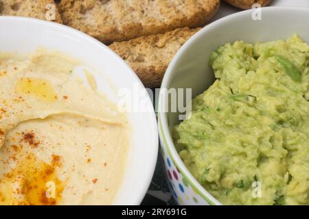 Ein sehr naher Schuss von zwei Schüsseln Dip, eine mit Hummus und eine mit Guacamole, beide aus frischen Zutaten. Die Brotstangen und der Toast sind raus Stockfoto