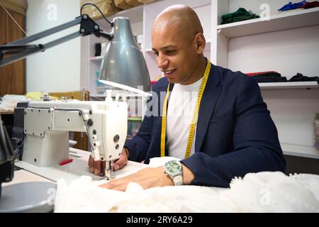 Fröhliche Schneiderin, die in der Werkstatt Kleider auf Bestellung herstellt Stockfoto