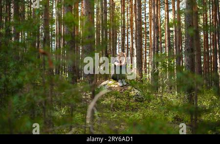 Waldbäder, die Gesundheit und Kraft am Wochenende wiederherstellen, Erwachsene Frau sitzt auf einem Felsvorsprung Stockfoto