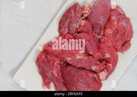 Fleischstücke auf einem Keramikbrett auf weißem Hintergrund. Rohes Rindfleisch zum Kochen. Draufsicht. Leerzeichen kopieren. Stockfoto