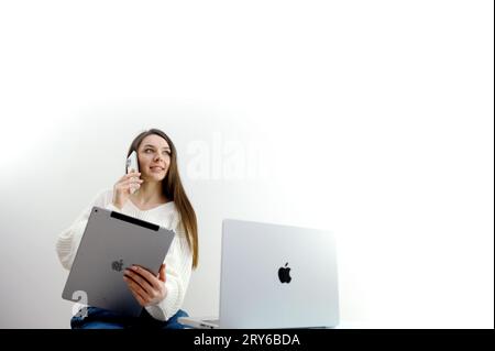 Geschäftsfrau, die macbook 14 Pro Smartphone und Apple New iPad Pro Tablet-pc mit Apple MacBook Pro Laptop-Computer auf Holztisch hält und verwendet Ukraine 09.28.2023 Stockfoto