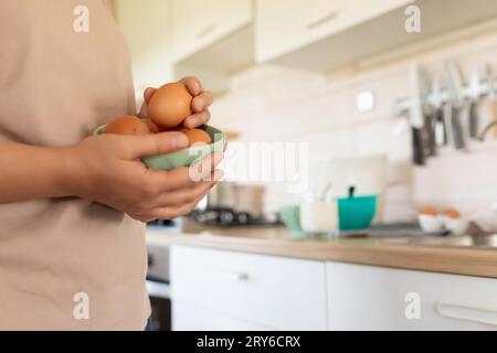 Eine Frau hält Hühnereier in einer Schüssel, während sie in der Küche steht Stockfoto