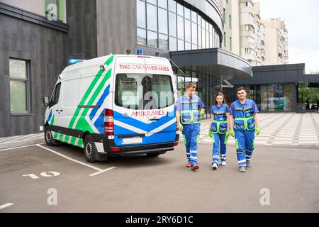 Ärzte in medizinischer Uniform laufen auf dem Parkplatz in der Nähe des modernen Gebäudes entlang Stockfoto