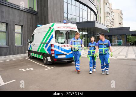 Menschen in medizinischen Uniformen laufen auf dem Parkplatz in der Nähe des modernen Gebäudes entlang Stockfoto