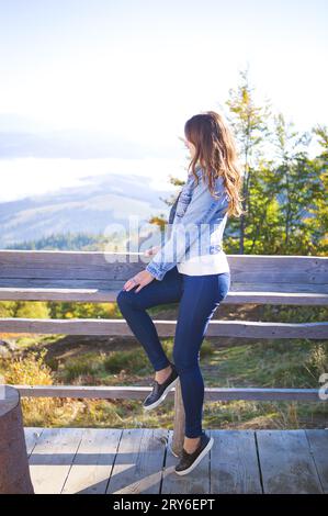 Das Mädchen sitzt auf einer Bank auf dem Berg in Pilipets und schaut auf den Nebel. Stockfoto