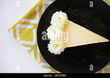 Cremige Käsekuchen mit weißen Blumen auf einem gelben Serviette geschmückt. Stockfoto