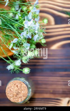 Nigella arvensis, Teufel im Busch, Liebe im Nebel in Holzmörtel, neben getrockneten Blumen in einem Medizingefäß mit Kork, aus dem schwarzes Kreuzkümmelöl hergestellt wird Stockfoto