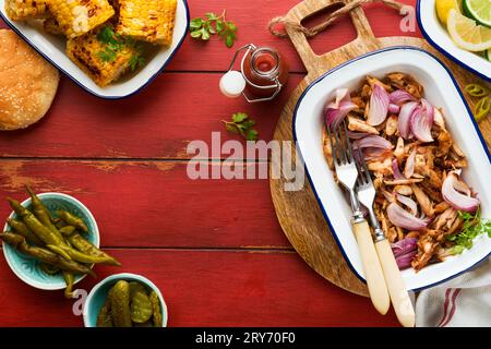 Gezapftes bbq-Hühnchen mit gebackenen Zwiebeln auf Servierplatte, bbq-Mais, Gurken, Chilischoten und Brötchen für Hot Dogs und Burger, Tomatensauce. Traditionell Stockfoto