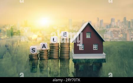 Würfel bilden das Wort „Verkauf“ auf Münzstapeln neben einem Musterhaus. Stockfoto