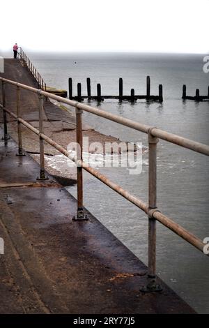 Einsame ältere Frau, die über Geländer zur Nordsee am Meer in overstrand im Norden von norfolk england blickt Stockfoto