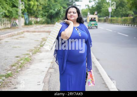 Junge indianerin in Übergröße, die Einkaufstaschen draußen auf der Straße hält. Übergewichtige Dame, die einkaufen geht. Stockfoto