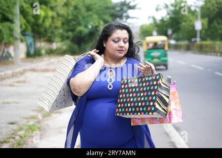 Junge indianerin in Übergröße, die Einkaufstaschen draußen auf der Straße hält. Übergewichtige Dame, die einkaufen geht. Stockfoto