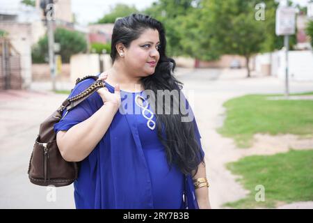 Junge indische Frau in Übergröße, die Lederhandtasche hält und draußen auf der Straße steht. Stockfoto