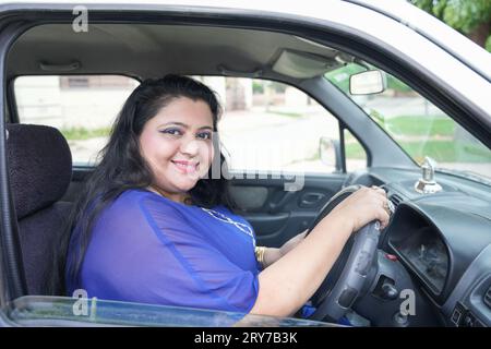 Glückliche indianerin in Übergröße, die im Auto sitzt, ohne den Sicherheitsgurt zu tragen und mit einem Lächeln auf die Kamera zu blicken. Stockfoto