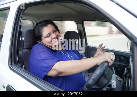Junge indianerin in Übergröße, die auf dem Handy spricht, während sie Auto fährt, ohne Sicherheitsgurt zu tragen, Sicherheitskonzept. Stockfoto