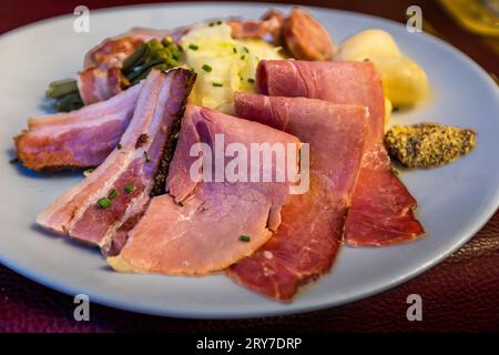 Das Hauptgericht auf der Kilbi-Karte ist Räucherschinken (Jambon de la Borne AOP), Speck und Sauccison mit Kohl. Das Fleisch wird traditionell im Kamin des Bauern gehängt und geräuchert. Sensler Brätzele and Jambon de la Borne AOP (Räucherschinken) ist ein Menü der Fribourg-Spezialität Kilbi. Das Kilbi oder Bénichon ist ein traditionelles Freiburger Festival. Freiburg - Freiburg, Schweiz Stockfoto