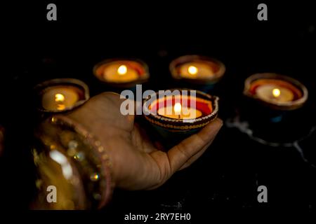 Happy Diwali - Frau Hände mit Henna halten brennende Kerze isoliert auf dunklem Hintergrund. Ton Diya Lampen während Dipavali, Hindu-Festival der Lichter ce beleuchtet Stockfoto