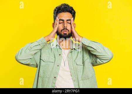 Unzufrieden erschöpfter indischer Hindu-Mann, der Schläfen reibt, um Kopfschmerzen zu heilen, leidet unter Spannung, Migräne, Stress, grimmigen Schmerzen, Bluthochdruck isoliert auf gelbem Hintergrund Stockfoto
