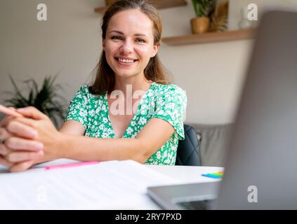 Porträt-Brünette Frau sitzt zu Hause am Schreibtisch, arbeitet freiberuflich, arbeitet von zu Hause aus. Stockfoto