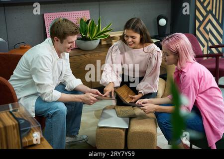 Zwei Frauen und ein Mann schauen sich Muster von Möbelmaterialien an, sie sitzen in weichen Stühlen Stockfoto