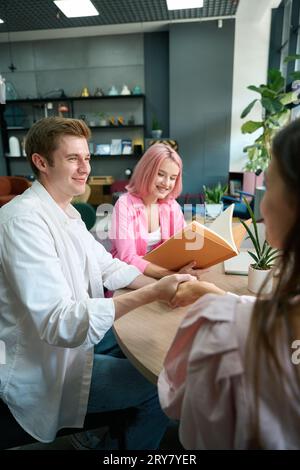 Der Typ dankt dem Manager mit einem Handschlag, seine Freundin sieht sich Kataloge am Tisch an Stockfoto