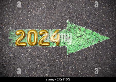 Grüner Pfeil auf Asphalt gemalt, Asphaltgrunge-Textur mit 2024 Goldzahlen, Neujahrsschild Stockfoto