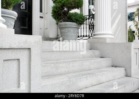 Historische weiße Veranda Betontreppen mit Topiary in Pflanzer mit schwarzer Tür und weißer Säule Stockfoto