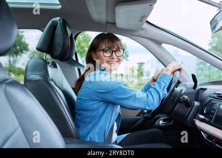 Eine Fahrerin mittleren Alters sitzt im Auto hinter dem Steuer und schaut lächelnd auf die Kamera Stockfoto