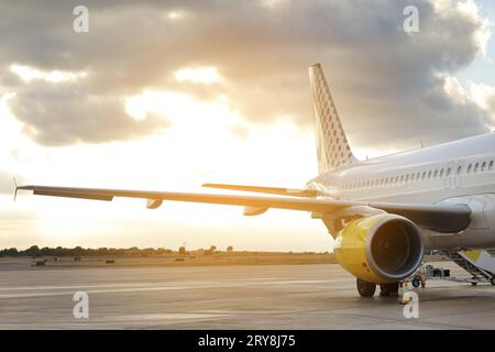Seitenansicht des Flugzeugflügels und des Triebwerks eines großen weißen Passagierflugzeugs, das am internationalen Flughafen des Terminals auf der Landebahn gegen den dramatischen Sonnenuntergang geparkt ist Stockfoto