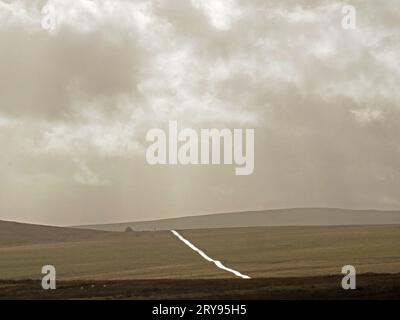 Silbernes Licht auf der nassen Straße wie ein Band, das sich über das nicht eingezäunte Moorland der Gaythorne-Ebene schlängelt und den dramatischen, stimmungsvollen Himmel in Eden Valley, Cumbria, England, Großbritannien Stockfoto