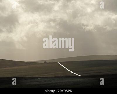 Silbernes Licht auf der nassen Straße wie ein Band, das sich über das nicht eingezäunte Moorland der Gaythorne-Ebene schlängelt und den dramatischen, stimmungsvollen Himmel in Eden Valley, Cumbria, England, Großbritannien Stockfoto