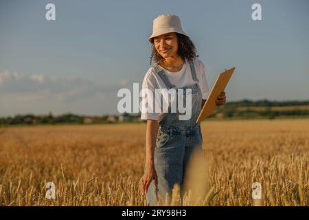 Lächelnde Farmerin mit Tablette auf einem Weizenfeld überprüft die Ernte. Landwirtschaftliches Konzept Stockfoto